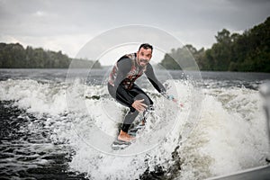 Active man is surfing on surfboard trails behind boat.