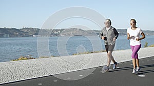 Active man and woman jogging on asphalt road along sea