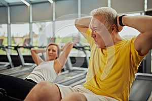 Active mature couple doing abdominal exercises together in modern fitness center, man and woman looks focused.