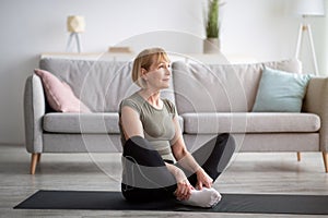 Active mature lady doing yoga, sitting in butterfly asana on sports mat at home, empty space