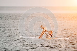 Active mature male paddler with his paddleboard and paddle on a sea at summer. Happy senior man stands with a SUP board