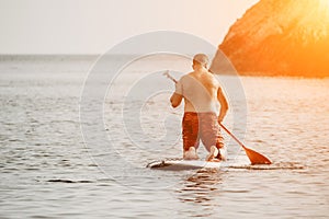 Active mature male paddler with his paddleboard and paddle on a sea at summer. Happy senior man stands with a SUP board