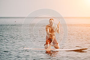Active mature male paddler with his paddleboard and paddle on a sea at summer. Happy senior man stands with a SUP board