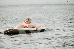 Active mature male paddler with his paddleboard and paddle on a sea at summer. Happy senior man stands with a SUP board