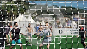 Active men playing soccer outdoors, view through net, healthy lifestyle, leisure