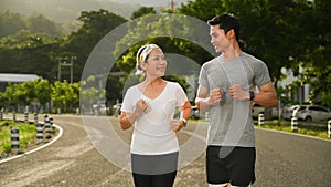 Active middle aged woman jogging with personal trainer at the park in evening. Healthy lifestyle and fitness concept