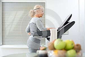 Active middle aged woman in sportswear using treadmill at home. Coronavirus Covid19 social distance.