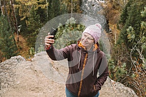An active middle-aged woman takes selfie with her smartphone while hiking in the mountains through the forest. Close up