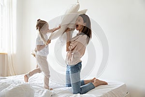 Active mother and daughter holding pillows fighting on bed