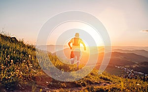 Active mountain trail runner dressed bright t-shirt with backpack running endurance marathon race by picturesque hills at sunset photo