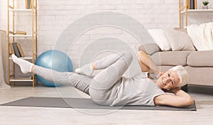 Sporty senior woman doing abs exercise on floor at home