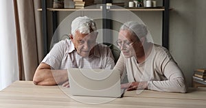 Active older married couple pensioners enjoy using laptop at home