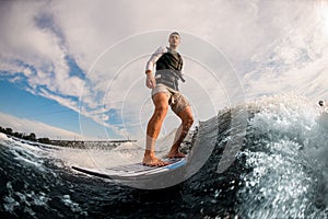 active one-armed man balanced on wakeboard through the waves from motorboat. Wakesurfing