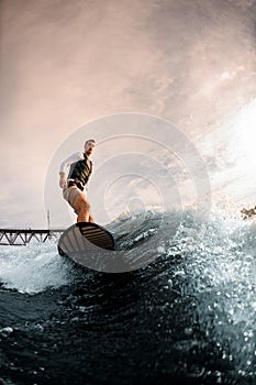 active one-armed sportsman standing on surfboard and rides the wave. Wakesurfing on the river