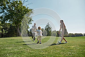 Active parents playing together with little boy child in green park on a summer day. Happy family enjoying leisure