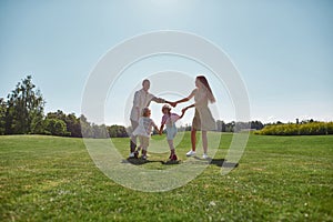 Active parents spending time together with two little kids, boy and girl in green park on a summer day. Happy family