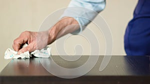 Active pensioner cleans the house, wipes dust with a rag from home furniture. Hands of an elderly person doing cleaning in the apa