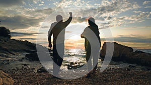 active pensioners, cheerful elderly man and woman having fun throwing stones into water while walking near sea coast