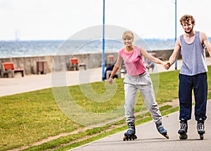 Young couple rollerblading in park holding hands.