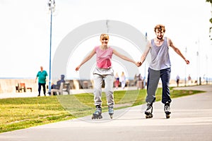 Young couple rollerblading in park holding hands.