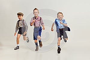 Active, playful boys, children playing together, running over grey studio background. After school fun. Joy. Concept of