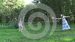 Active pregnant woman with girl play badminton game in park