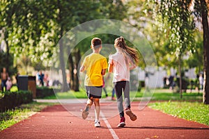 Active recreation and sports children in pre-adolescence. Caucasian twins boy and girl 10 years old jogging on red rubber track