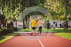 Active recreation and sports children in pre-adolescence. Caucasian twins boy and girl 10 years old jogging on red rubber track