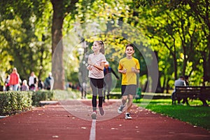 Active recreation and sports children in pre-adolescence. Caucasian twins boy and girl 10 years old jogging on red rubber track