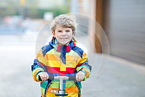 Active school kid boy in colorful casual clothes riding with his scooter in the city