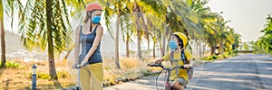 Active school kid boy and his mom in medical mask and safety helmet riding a bike with backpack on sunny day. Happy