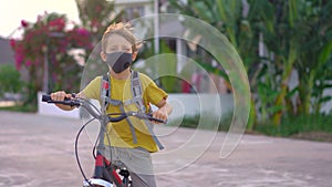 Active school kid boy in medical mask riding a bike with backpack on sunny day. Happy child biking on way to school. You