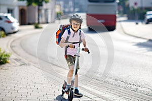 Active school kid boy in safety helmet riding with his scooter in the city with backpack on sunny day. Happy child in