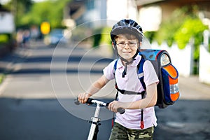 Active school kid boy in safety helmet riding with his scooter in the city with backpack on sunny day. Happy child in