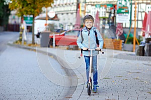 Active school kid boy in safety helmet riding with his scooter in the city with backpack on sunny day. Happy child in