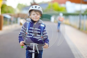 Active school kid boy in safety helmet riding with his scooter in the city with backpack on sunny day. Happy child in