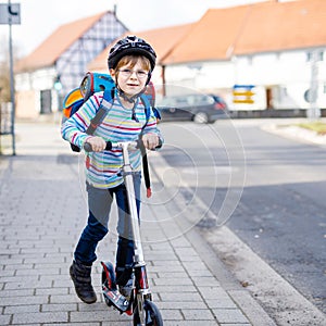 Active school kid boy in safety helmet riding with his scooter in the city with backpack on sunny day. Happy child in