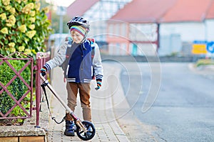 Active school kid boy in safety helmet riding with his scooter in the city. Happy child in colorful clothes biking on
