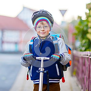 Active school kid boy in safety helmet riding with his scooter in the city. Happy child in colorful clothes biking on