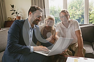 Active senior couple discussing with real estate agent over laptop in living room