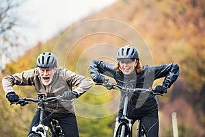 Active senior couple with electrobikes cycling outdoors on a road in nature.