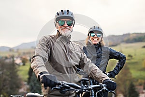 Active senior couple with electrobikes standing outdoors on a road in nature. photo