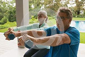 Active senior couple exercising with dumbbell in porch at home