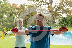 Active senior couple exercising with resistance band in porch at home