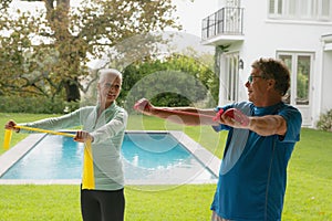 Active senior couple exercising with resistance band in porch at home