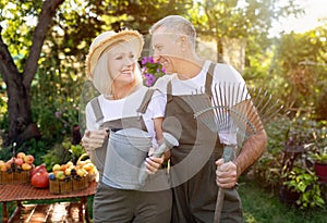 Active senior couple holding gardening tools, working together in their garden at sunny day