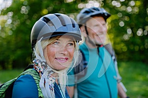 Active senior couple riding bicycles at summer park, woman with bicycle helmet, healthy lifestyle concept.