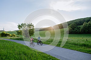 Active senior couple riding electric bicycles on trail at summer park, healthy lifestyle concept.