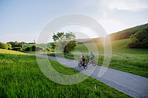 Active senior couple riding electric bicycles on trail at summer park, healthy lifestyle concept. Rear view.