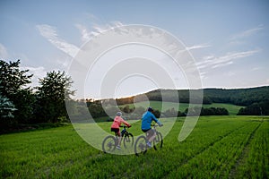 Active senior couple riding electric bicycles on trail at summer park, healthy lifestyle concept. Rear view.